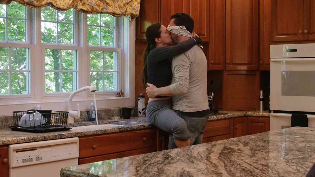 A women sits on the kitchen counter kissing a man passionately